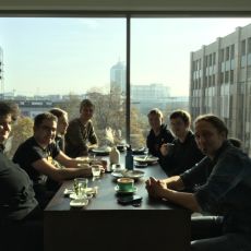 IndieWebCamp Düsseldorf folks sitting at a table in front of a window for lunch.