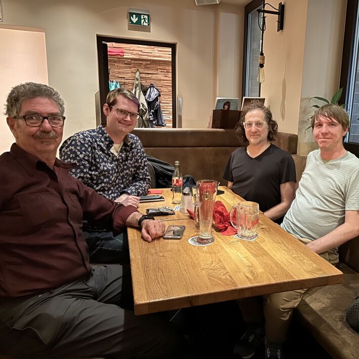 Four people seated at a table with drinks inside a restaurant near the entrance.