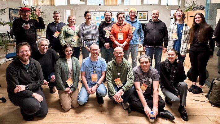 17 people gathered inside an office space smiling for a group photo.