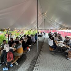 Large group of people at several tables under a large white tent.